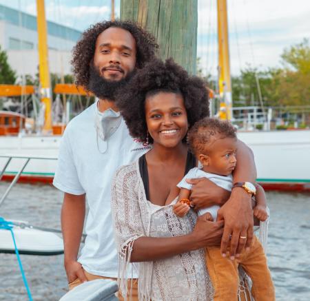 A black husband and wife hold their baby by the water