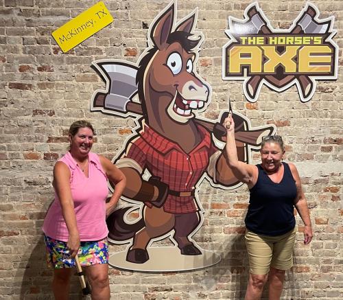 Tw women with axes in front of Horse's Axe sign