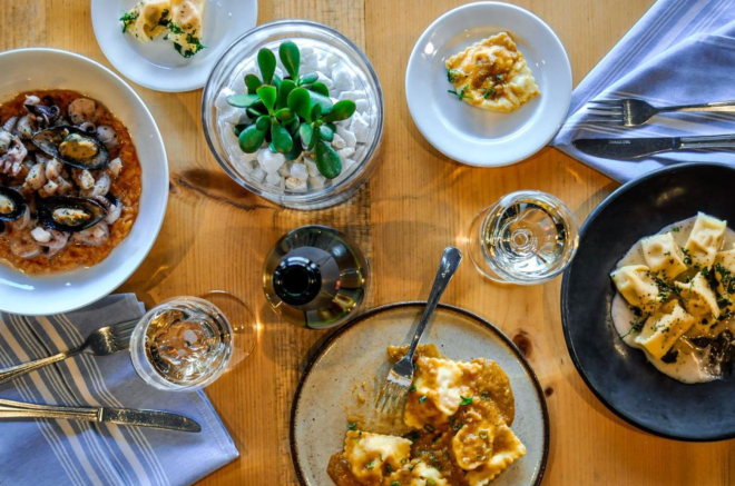 Aerial view of table with five plates of pasta and two glasses of water on top.