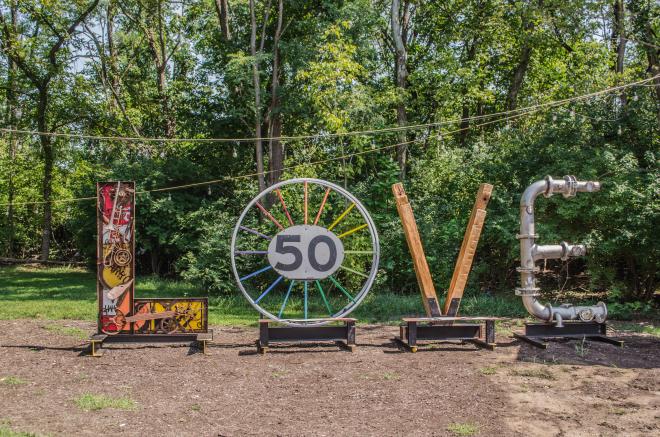 Large letters make up the word 'LOVE' as part of an installation at Black Dog Salvage. The L is made of industrial elements and musical instruments, the O is made of two industrial spools painted in the colors of the rainbow, the V is made of reclaimed pine beams, and the E is made from stainless steel piping.