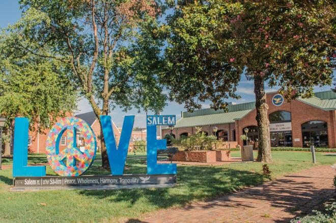 'LOVE' is spelled out in 6-ft tall blue letters. The 'O' is a peace sign filled in with colorful handprints.