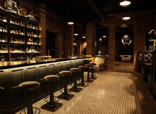Interior of a dimly lit speakeasy bar with a white tile floor and vintage decor.