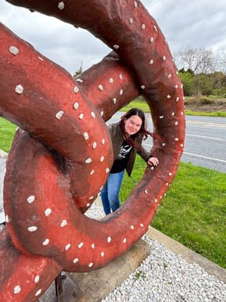 A young woman looks through a loop of a giant pretzel at Tom Sturgis