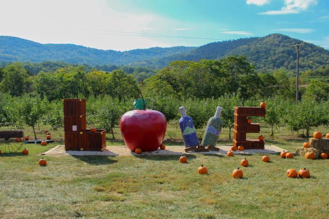 LOVEworks at Peaks of Otter Winery with Blue Ridge Mountains in the background. 'L' and 'E' are made out of produce crates, 'O' is an apple, and two wine bottle sculptures make the 'V'