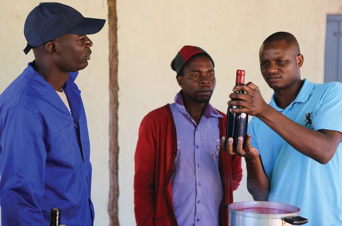 Three black men look at a bottle of wine