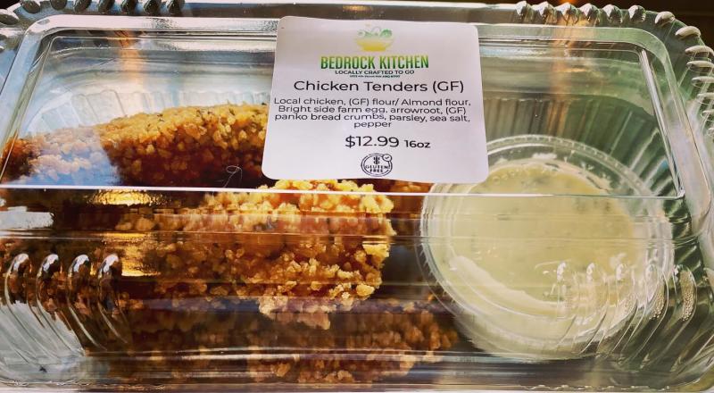 Some chicken tenders and dipping sauce in a plastic container from Bedrock Kitchen.