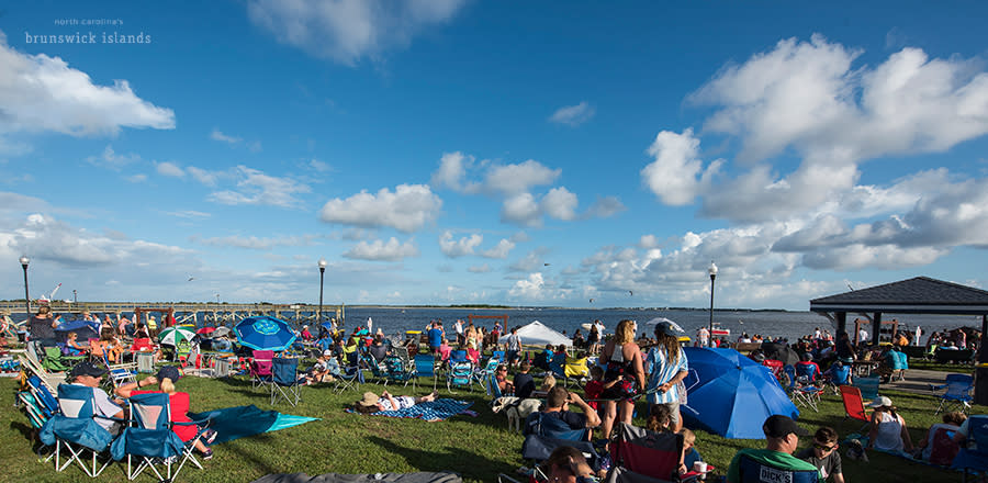 a group of people setting up blankets and chairs to watch an evening firework display in Southport, NC for the NC 4th of July Festival