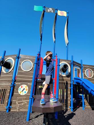 boy stands saluting on plank of pirate ship playground