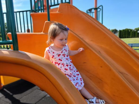 toddler girl in a dress going down an orange slide