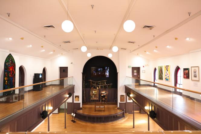 A view of an art gallery from the 2nd level mezzanine looking towards a stage with an installation