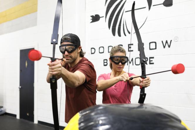 A man and woman wearing goggles and preparing to launch blunt arrows using bows