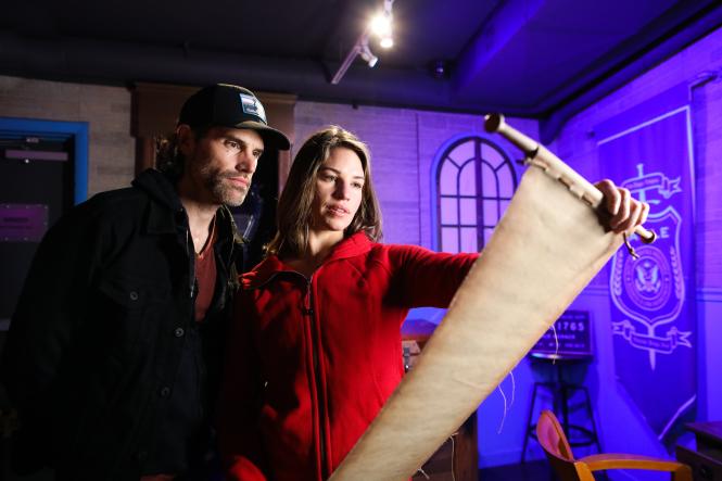 A man and woman studying a scroll within an escape room