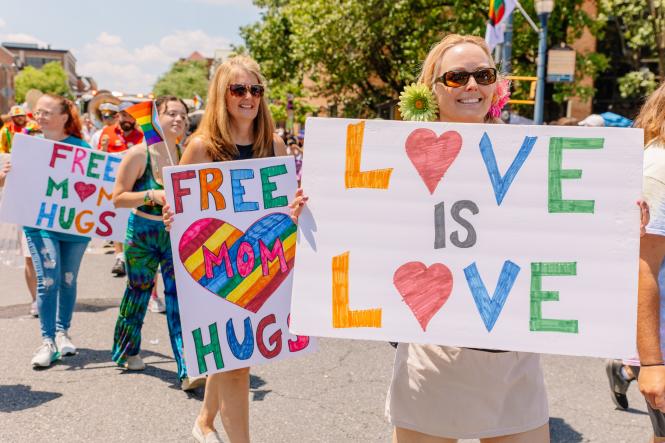 People march in the Annapolis Pride Parade holding banneres and signs about LGBTQIA+ rights