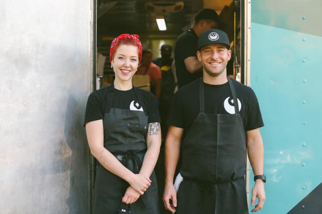 A woman and a man - owners of Black Market Bakers stand in front of a food truck