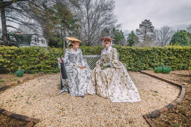 Two women in period costume sitting in a historic garden