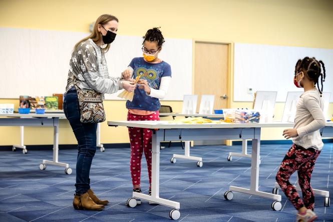 Two young black girls and an older white woman take part in a craft at a local library.