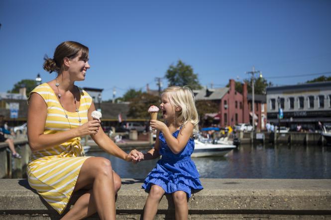 A woman and child sit by the water eating ice cream