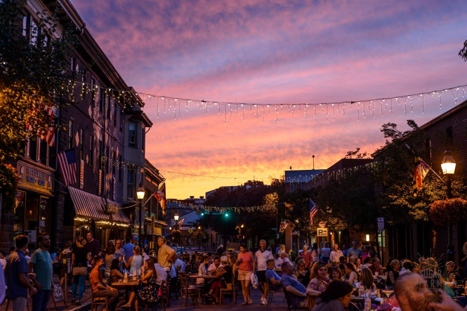 A street with dining tables and people, twinkle lights hung up during a sunset in Annapolis