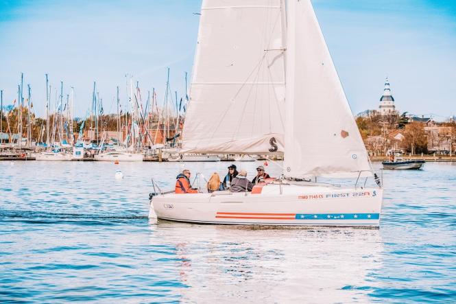 A group of people sailing on a sailboat with the City of Annapolis in the background