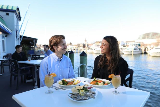 A man and woman eat seafood by the water's edge