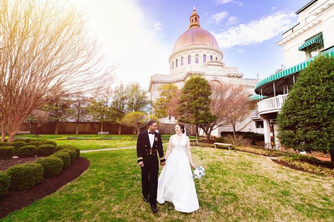 a bride and groom holding hands in front of a chapel dome in the naval academy in Annapolis