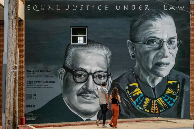 two people walking past a mural of Justices Marshall and Ginsberg