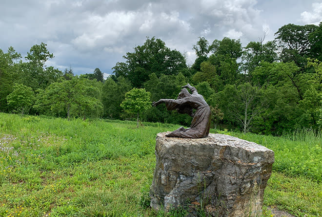 bronze sculpture of a girl on a stone base in a park