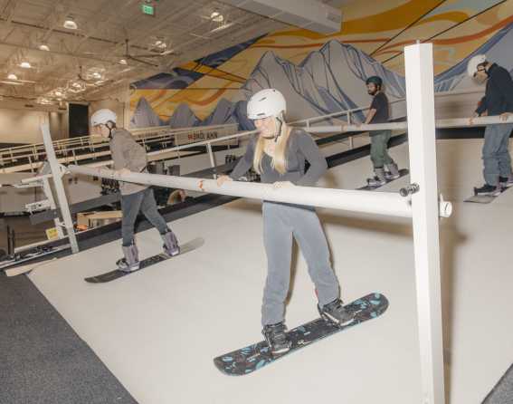Several people learning to snowboard on Snobahn's indoor slope simulator.