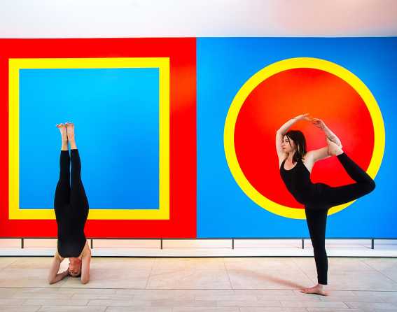 Two people doing yoga in front of large paintings at the ART Hotel Denver, Curio Collection by Hilton, in Denver, Colorado.