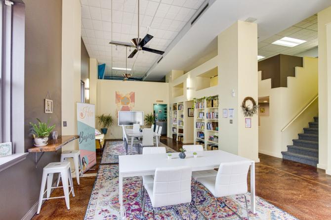 A bright room with two white tables with white chairs, white bookcases on one side and windows on the other at The Hive in Wichita, KS