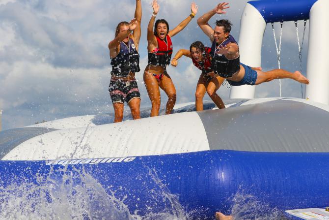 Four teenagers jump on a giant inflatable platform in the water