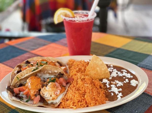 Plate with two shrimp tacos, rice and beans sprinkled with cheese