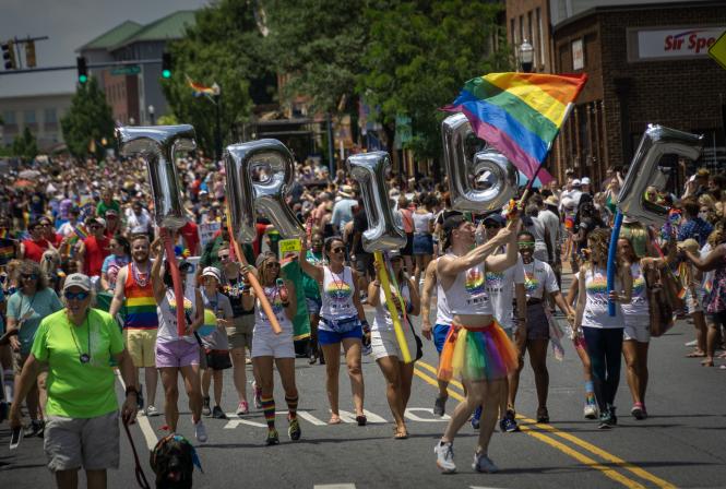 A mass of people at the Annapolis Pride Parade hold a 'TRIBE' balloon sign.