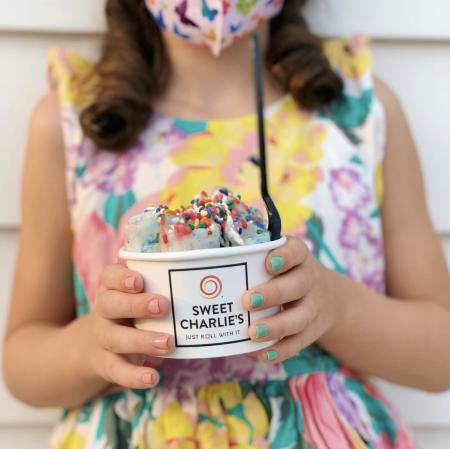 A woman in a flowered dress holds a cup of vegan ice cream with sprinkles from Sweet Charlie's in Huntsville, AL.