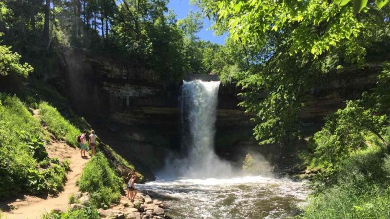 Two hikers stand along the path on the left admiring Minnehaha Falls