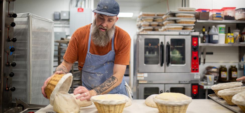 Bearded man in blue apron making bread