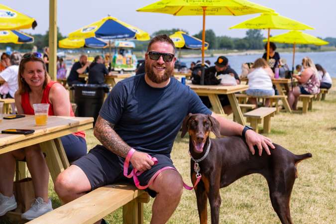 A dog is pictured with his owner at the Lake Andrea Beer Garden in Pleasant Prairie. The lake is visible in the background, with the yellow umbrellas and picnic tables showing as well.