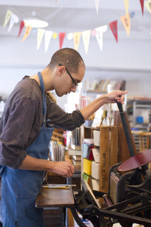 Man in apron working at lettlerpress machine at Igloo letterpress