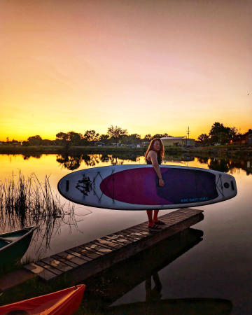 Woman holding paddleboard in front of a sunset