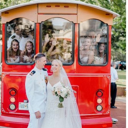A couple poses in front of their wedding party aboard a trolley.