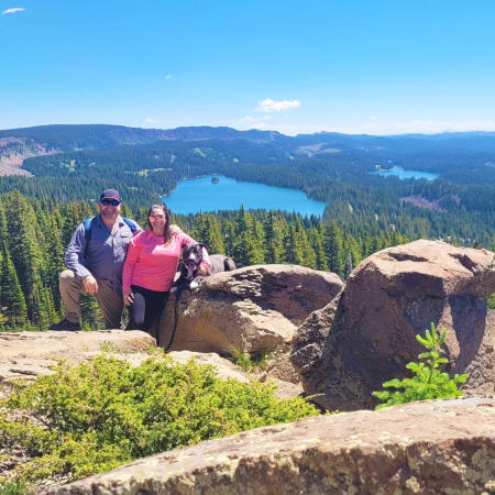 Two People and a dog posing in front of a view of the Grand Mesa
