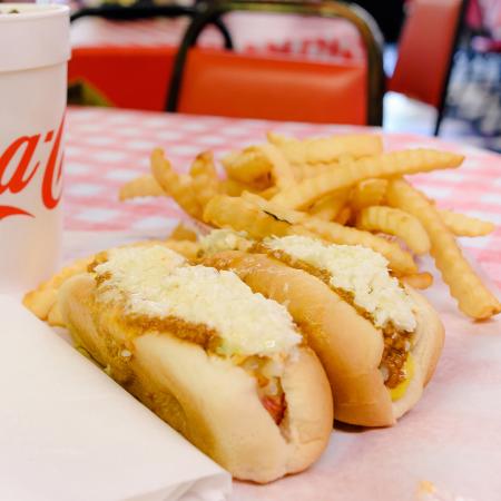 Two red hot dogs all the way laid out with fries, onion rings, and a Coke