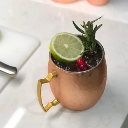 Moscow Mule in a copper cup on a counter with lime, crandberry, and rosemarry garnish.