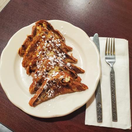 Deliciously powdered french toast on a white plate sitting on a wooden table at Tucci’s Family Diner.