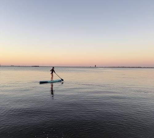 A girl paddleboarding on the Delaware Bay at sunset.