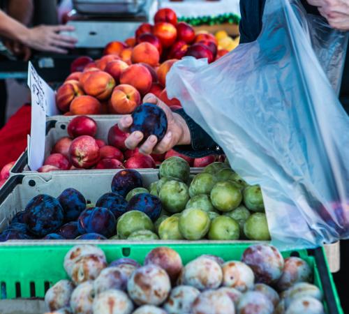 Person grabs plum from fruit stand to place into basket