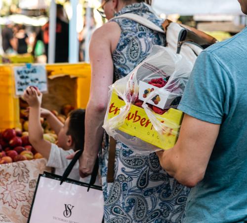 Man carrying box of strawberries near fruit stand