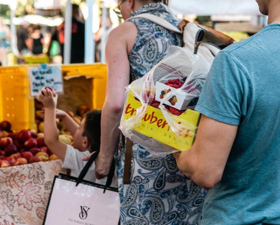 Man carrying box of strawberries near fruit stand