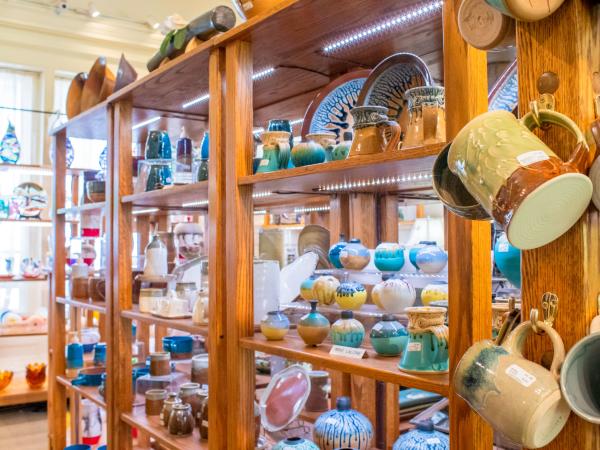 A wooden shelf is filled with colorful pottery; hanging mugs, bowls, and plates.