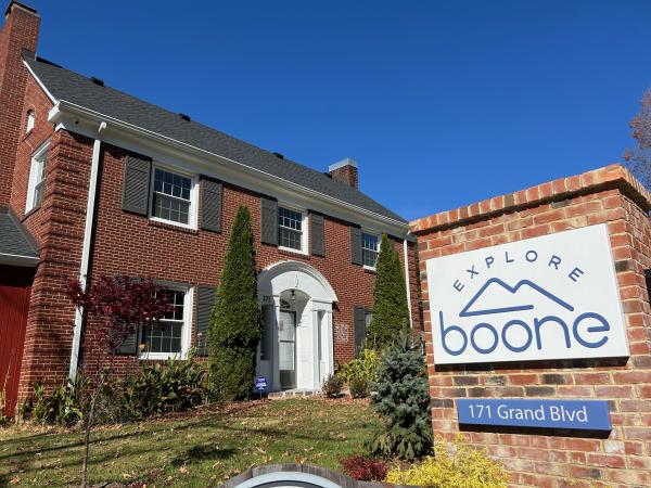 A sign for Explore Boone's visitors center and office is in front of a large brick house.
